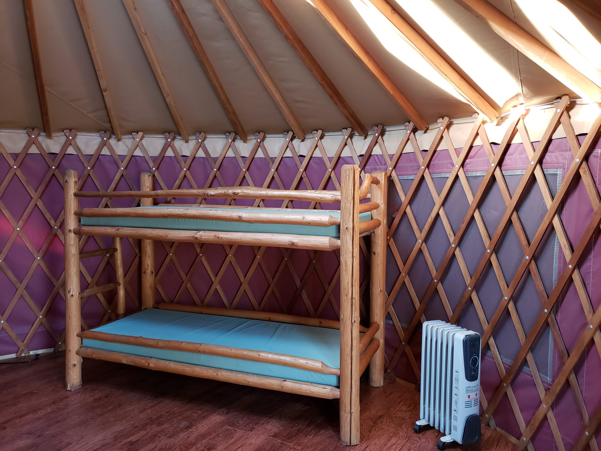 Interior of a yurt with wooden bunk beds and a portable heater.