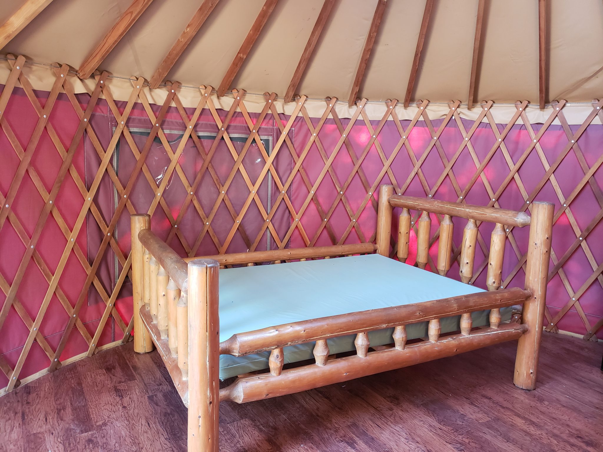 Log bed with mattress inside a yurt with lattice walls.