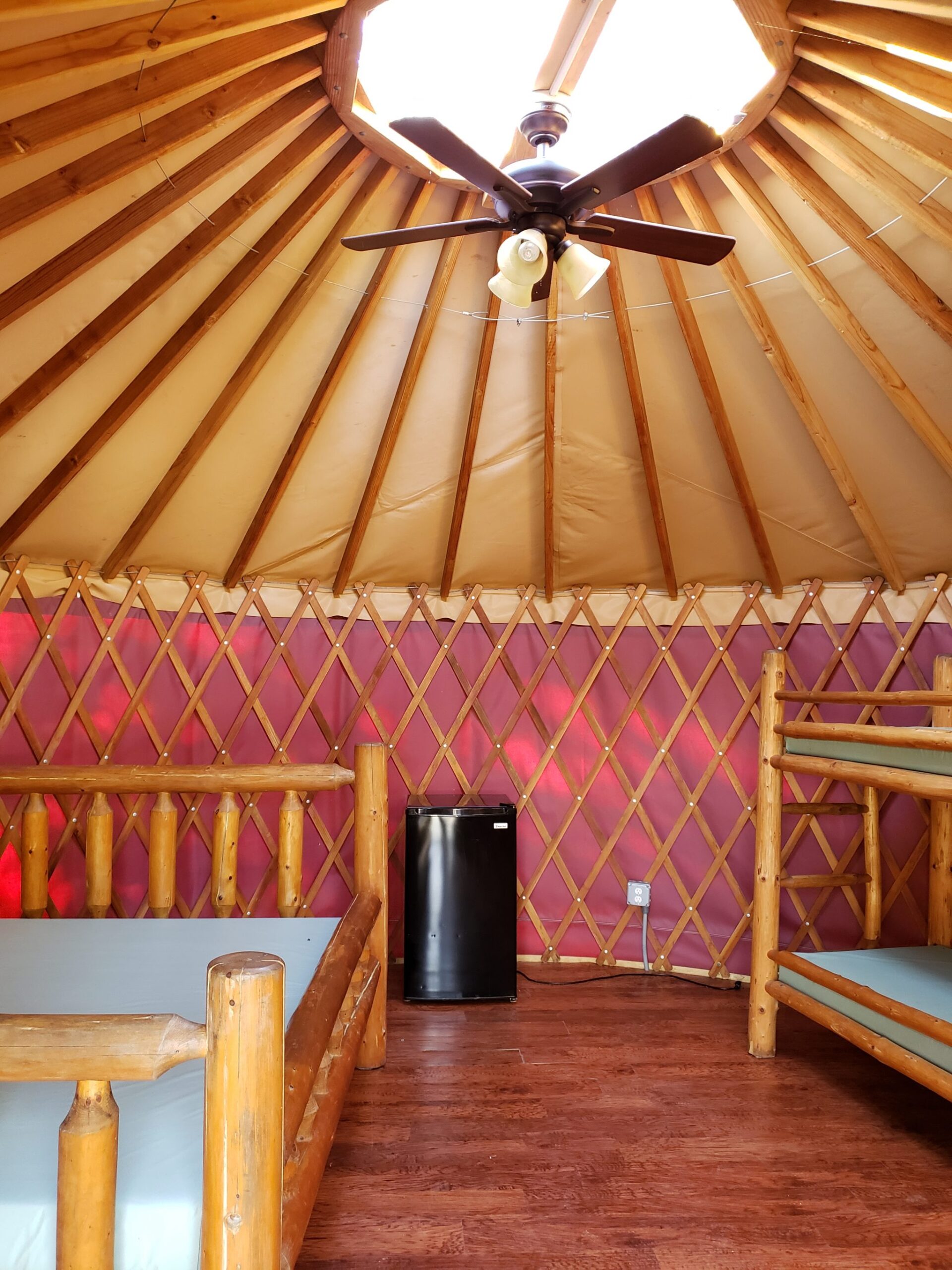 Interior of a yurt with bunk beds, mini-fridge, ceiling fan, and skylight.