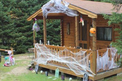 Wooden cabin decorated for Halloween with fake spiderwebs, pumpkins, and witch figures.