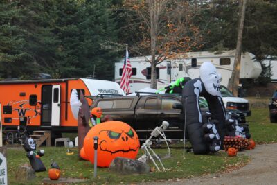 Halloween decorations at a campsite with RVs, including inflatable pumpkins, skeletons, and a ghost arch.
