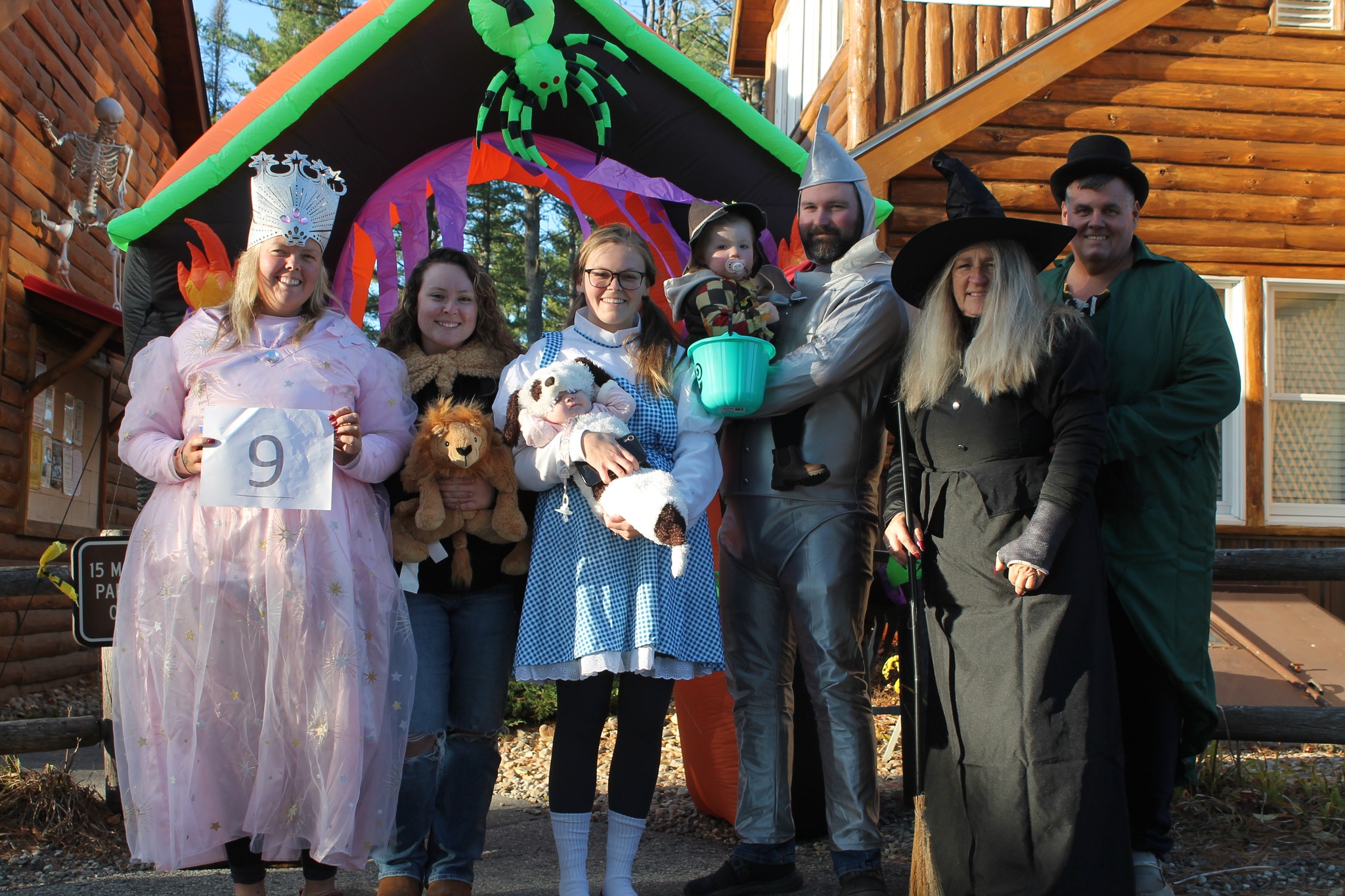 Group in Wizard of Oz costumes poses for Halloween, including Dorothy, Tin Man, and Wicked Witch.