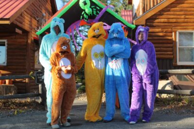 Five people in Care Bear costumes: blue, brown, yellow, blue, and purple.