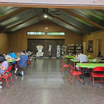 People gathered at tables in a large hall with wooden doors and a metal ceiling.