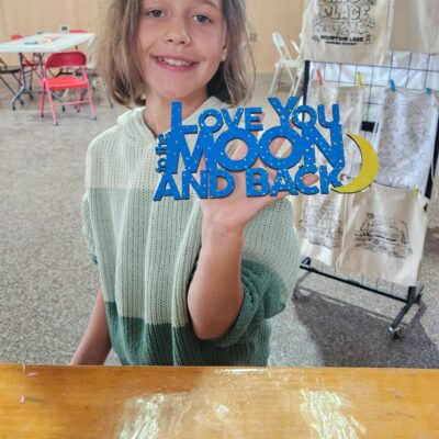 Girl holds blue "Love You to the Moon and Back" sign with yellow moon.