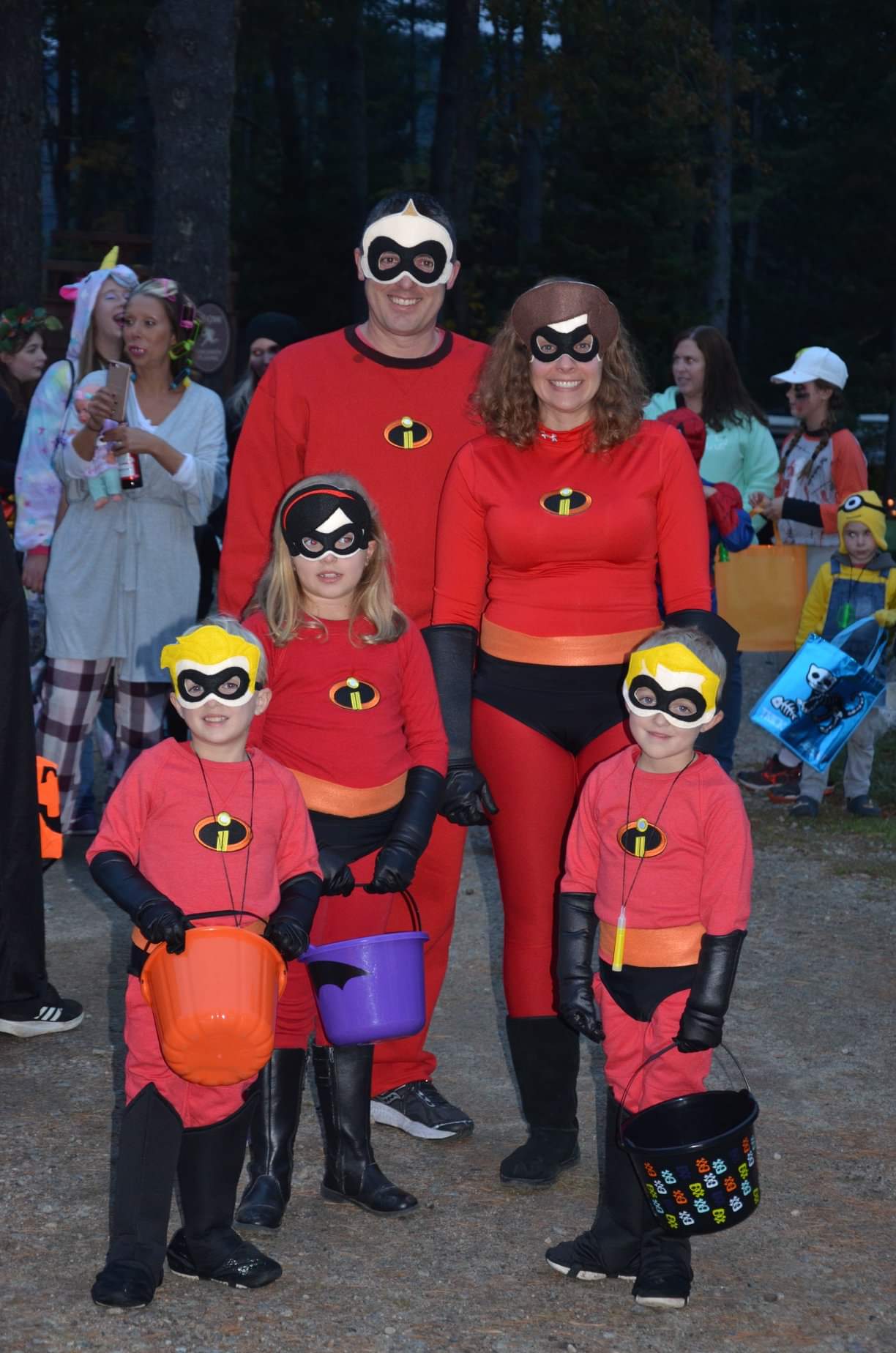Family dressed as the Incredibles for Halloween, holding candy buckets.