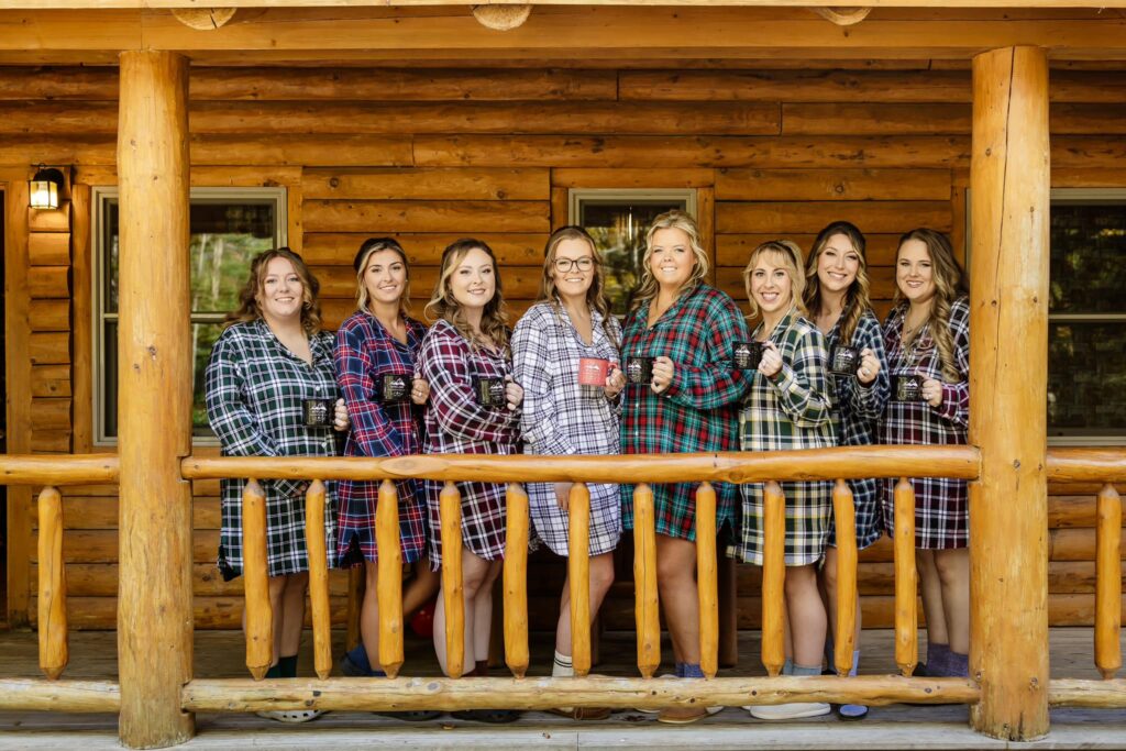 Bridal party in matching flannel pajamas holding mugs on a cabin porch.