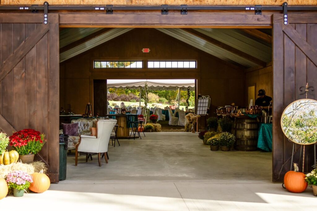 Barn venue with open doors, pumpkins, fall decor, and outdoor tent reception.