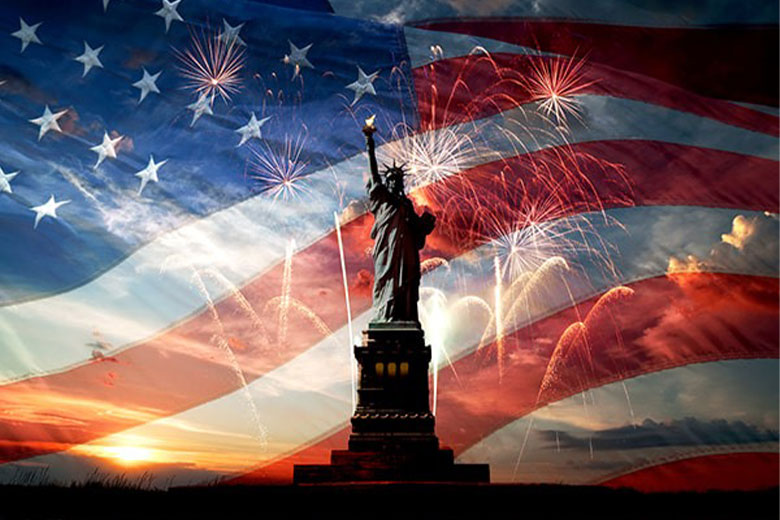 Statue of Liberty with fireworks and American flag at sunset.
