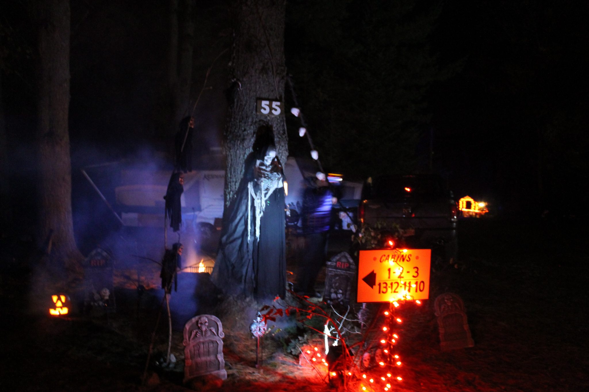 Spooky Halloween decorations with grim reaper, tombstones, and orange lights at night.