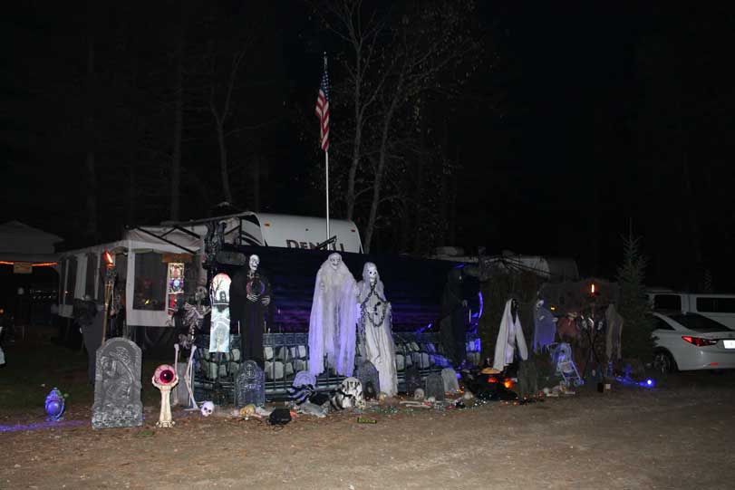Spooky Halloween decorations with ghosts, skeletons, and tombstones at a campsite at night.