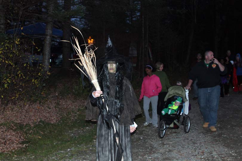 Person in witch costume holding broomstick at night with people in background.