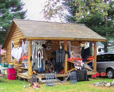 Log cabin decorated for Halloween with skeletons, ghosts, and spooky figures.