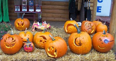 Assortment of carved Halloween pumpkins with spooky faces and designs on hay bales.