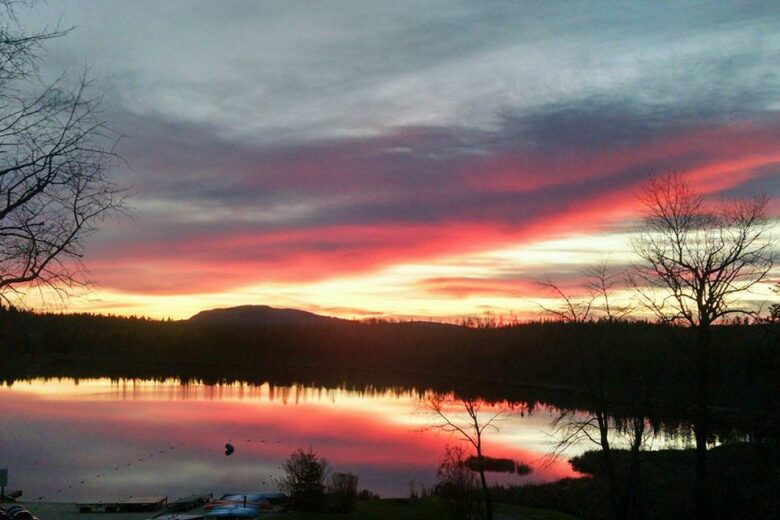 Vibrant pink and orange sunset over a calm lake with silhouetted trees and hills.